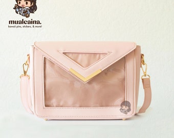 May include: A light pink crossbody bag with a clear plastic flap and gold accents. The bag has a gold chain strap and a small gold charm.