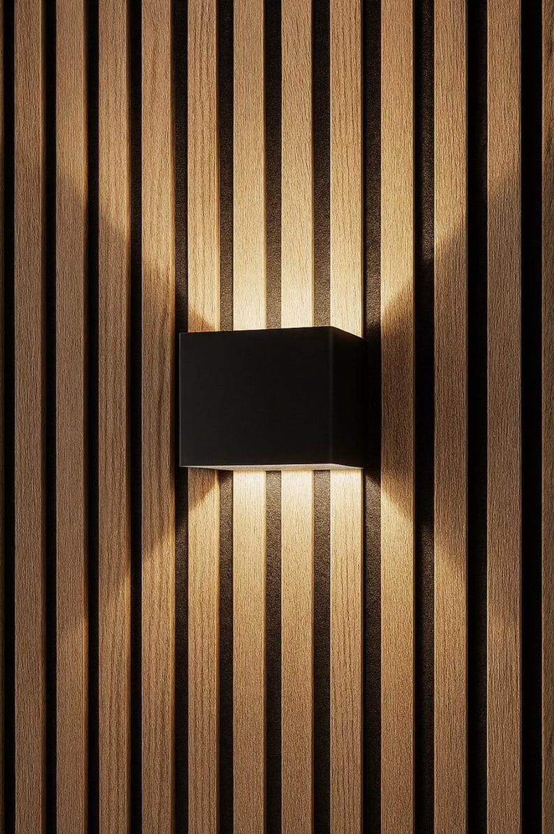May include: A modern black square wall sconce mounted on a vertical wood slat wall. The sconce emits a warm light, creating a contrast with the dark wood grain. The design is minimalist and contemporary.