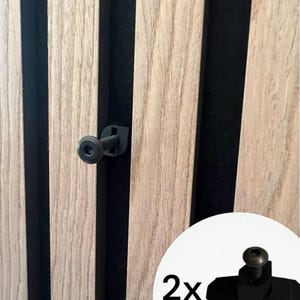 Könnte beinhalten: Zwei schwarze Wandmontage-Clips aus Kunststoff zum Befestigen von Holzpaneelen. Die Clips haben einen Schraubenkopf und eine hakenartige Form. Die Clips sind vor einem Hintergrund aus Holzpaneelen abgebildet.