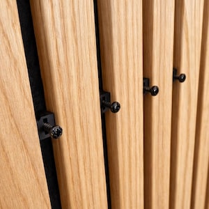 Könnte beinhalten: Nahaufnahme einer Holzlattenwand mit schwarzen Schrauben und Befestigungsmaterial. Die vertikalen Holzlatten sind hellbraun mit sichtbarer Holzmaserung. Der Hintergrund ist dunkelgrau oder schwarz.