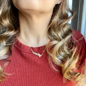 May include: A woman wearing a red shirt with a gold necklace that says "worthy".