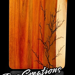 Puede incluir: Una tabla de cortar de madera con un acabado de grano de madera natural y un diseño de rayo negro. La tabla tiene un asa y el texto "Tico Creations" está impreso en la parte inferior.