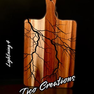 Puede incluir: Una tabla de cortar de madera con un diseño de rayo negro. La tabla tiene un asa y el texto "Tico Creations" está escrito en la parte inferior.
