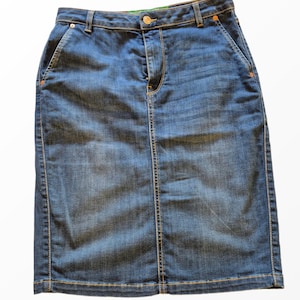 May include: A knee-length blue denim skirt featuring a high-waisted design with a button and zipper closure, belt loops, two side pockets, and contrasting orange stitching along the seams and hemline, presented against a plain white background.