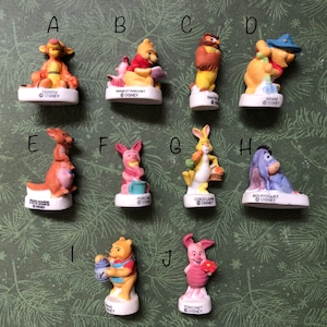 Könnte beinhalten: Eine Sammlung von zehn Disney-Figuren mit Charakteren aus Winnie Puuh. Die Figuren, darunter Tigger, Ferkel und Eeyore, stehen auf weißen Sockeln. Jede Figur ist in leuchtenden Farben bemalt.