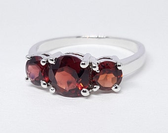 May include: A silver ring with three red garnet stones set in a row.