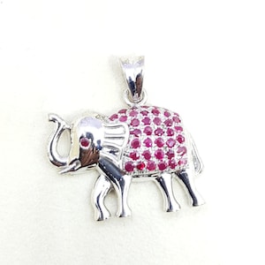 Puede incluir: Colgante de plata con forma de elefante adornado con piedras de rubí rojo. El elefante está de pie con la trompa levantada y tiene un diseño detallado.