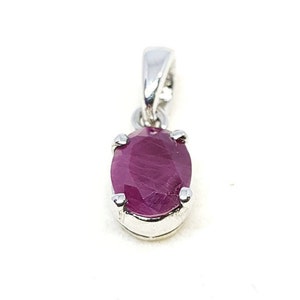 Può includere: Un ciondolo d'argento con una pietra preziosa ovale di rubino rosso scuro.