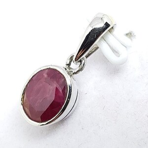 May include: A silver pendant with a red oval gemstone. The pendant has a simple design and is perfect for adding a touch of elegance to any outfit.