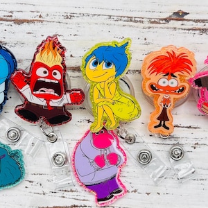 May include: Set of nine colorful character badge reels featuring characters from the animated film Inside Out. The characters include Joy, Sadness, Anger, Fear, Disgust, Bing Bong, and a few others.