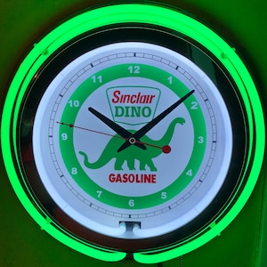 May include: A round wall clock with a green neon light border. The clock face is white with black numbers and hands. The Sinclair Dino logo and the word "GASOLINE" are in green. The clock is approximately 12 inches in diameter.