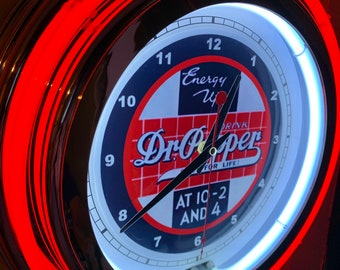 May include: A circular neon Dr. Pepper clock with a red and black outer ring. The clock face displays the Dr. Pepper logo and the text "AT 10-2 AND 4". The clock has a white neon inner ring and black clock hands.