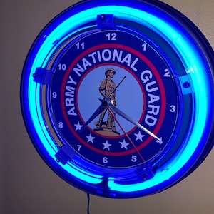 May include: A round wall clock with a blue neon light border. The clock face is navy blue with the words "ARMY NATIONAL GUARD" and a soldier graphic. The clock hands are silver.