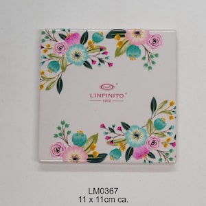 May include: White ceramic coaster with a floral design featuring pink, blue, and green flowers. The coaster has the text "L'Infinito 1972" in the center. The coaster measures 11 x 11 cm.
