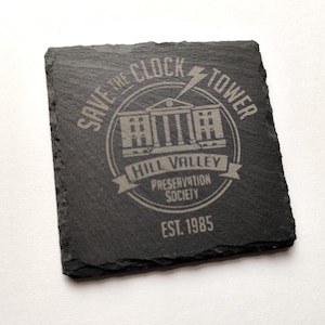 May include: Square black slate coaster with etched design. The design includes the text "SAVE THE CLOCK TOWER" around a building illustration, with "HILL VALLEY PRESERVATION SOCIETY" and "EST. 1985" below.