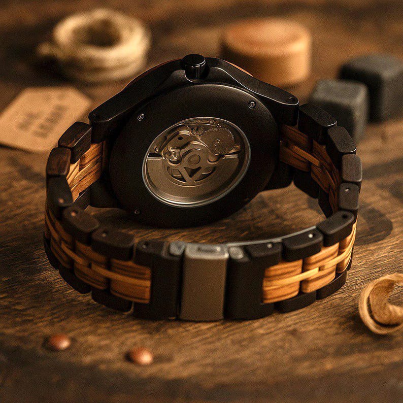 May include: A wristwatch featuring a black circular case with an exposed mechanical movement on the back. The band is constructed from alternating links of dark black wood and light tan wood, secured by a metallic silver-toned folding clasp.