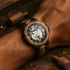 May include: A wristwatch featuring a round wooden bezel with Roman numerals and a black dial revealing internal mechanical gears. The band combines black links with central wooden accents. The text "BE IT MOST LA NOT UVIRE" is engraved on the bezel.