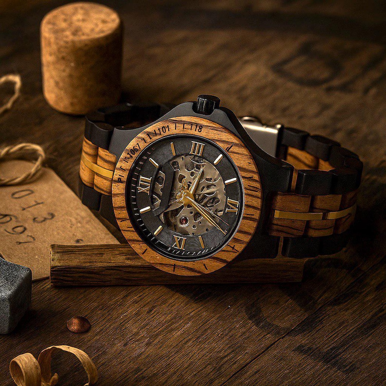 May include: A wristwatch featuring a round wooden bezel with Roman numerals and a skeleton dial revealing internal mechanical gears. The band is constructed from alternating black and wood-grain links with a gold-tone center accent line.
