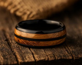May include: A ring featuring a polished black band with a central inlay of natural brown wood grain. The design includes a thin black stripe running horizontally through the center of the wood, creating a layered appearance with smooth edges.