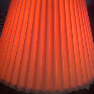 May include: A red pleated lampshade with a gold base. The lampshade is made of fabric and has a soft, warm glow.
