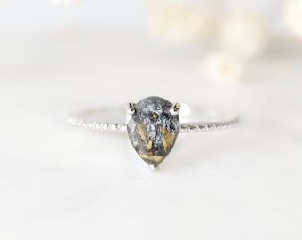 May include: A silver ring with a pear-shaped black and gold gemstone.