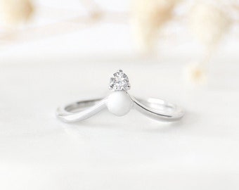 May include: A silver ring with a white pearl and a small diamond accent. The ring is shaped like a V.