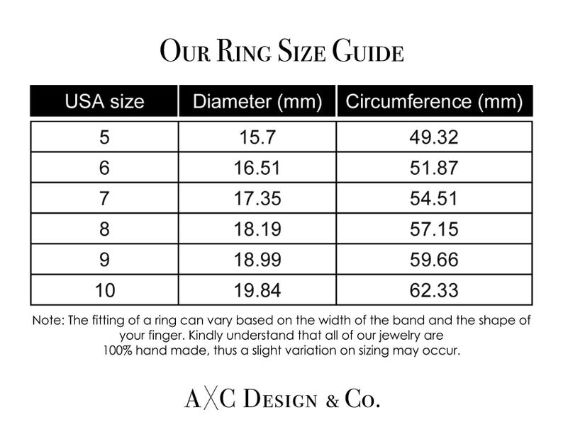 May include: A white ring size guide with black text. The guide includes USA ring sizes 5 through 10, with corresponding diameter and circumference measurements in millimeters. The text "OUR RING SIZE GUIDE" is at the top.