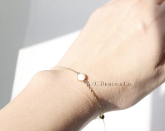 May include: A delicate gold chain bracelet with a single white round stone charm. The bracelet has an adjustable sliding clasp.