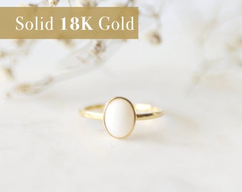 May include: A simple gold ring with a white oval gemstone. The ring is made of solid 18K gold.