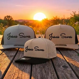 Puede incluir: Tres gorras de b&eacute;isbol con corona estructurada y visera plana. Cada gorra presenta el texto "Jesus Saves" bordado en letra cursiva negra en el panel frontal. Las gorras son de tonos beige y arena con detalles en color negro.