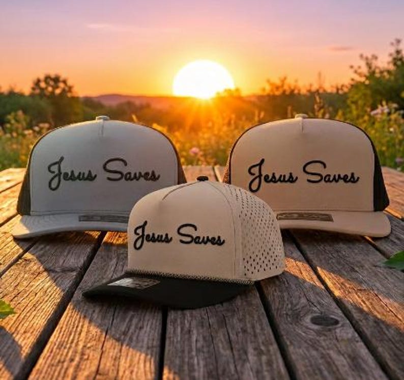 Puede incluir: Tres gorras de b&eacute;isbol con corona estructurada y visera plana. Cada gorra presenta el texto "Jesus Saves" bordado en letra cursiva negra en el panel frontal. Las gorras son de tonos beige y arena con detalles en color negro.