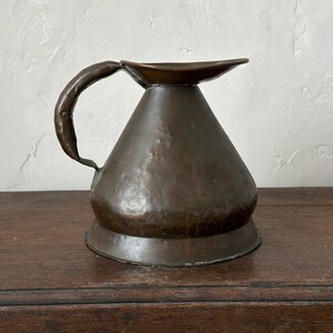May include: A hammered copper pitcher with a wide, rounded base and a flared spout. The pitcher has a single, curved handle.