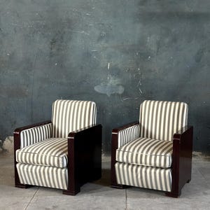 May include: Two matching armchairs with dark wood frames and striped cushions. The cushions feature vertical gray and white stripes. The armrests and frames are a dark, rich wood color. The chairs are set against a dark gray wall.