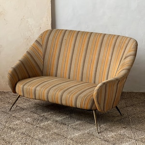 May include: A striped fabric sofa with a curved back and thin metal legs. The sofa is sitting on a woven rug.