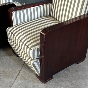 May include: A vintage armchair with a dark wood frame and striped cushions. The cushions feature vertical gray and white stripes. The armrests and frame have a glossy finish. The chair is a classic piece of furniture.