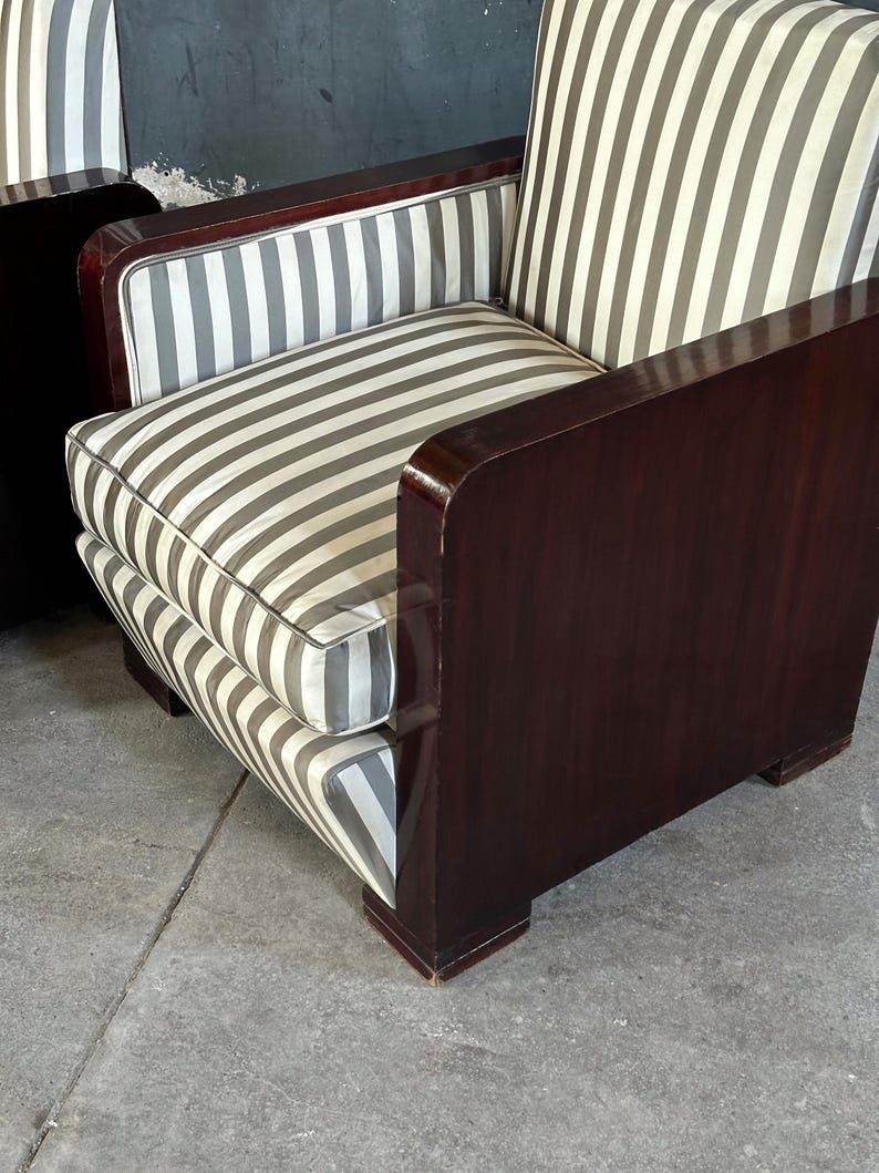 May include: A vintage armchair with a dark wood frame and striped cushions. The cushions feature vertical gray and white stripes. The armrests and frame have a glossy finish. The chair is a classic piece of furniture.