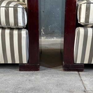 May include: Two armchairs with dark wood frames and striped cushions. The cushions have a pattern of alternating white and gray stripes. The wood frames are a deep, rich brown color. The armchairs are positioned close together.