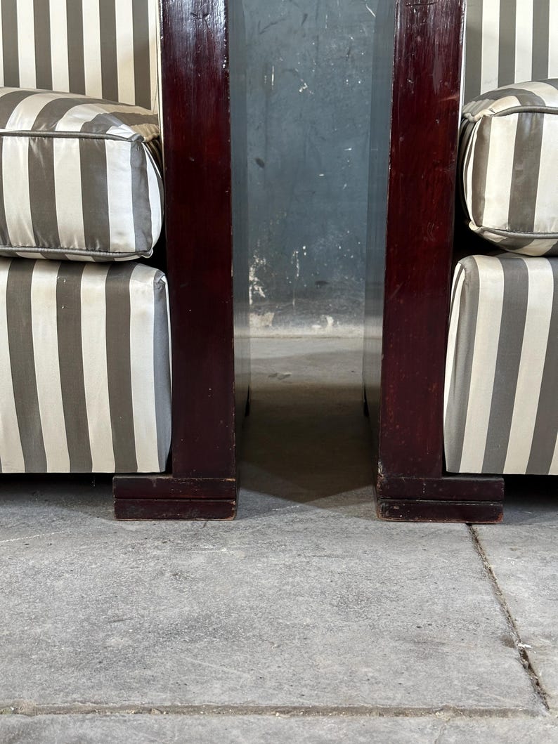 May include: Two armchairs with dark wood frames and striped cushions. The cushions have a pattern of alternating white and gray stripes. The wood frames are a deep, rich brown color. The armchairs are positioned close together.