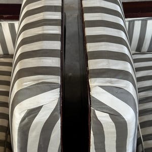 May include: Close-up of two antique chairs with striped upholstery. The fabric features alternating bands of gray and white. The wooden frames have a dark, polished finish. The chairs are positioned close together.