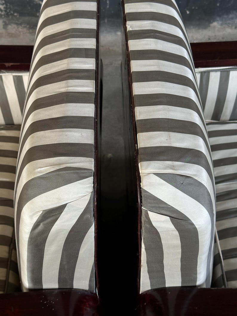 May include: Close-up of two antique chairs with striped upholstery. The fabric features alternating bands of gray and white. The wooden frames have a dark, polished finish. The chairs are positioned close together.