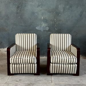 May include: Two matching armchairs with a striped pattern in shades of gray and white. The chairs have dark wood frames and armrests. The background is a textured, dark gray wall.