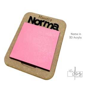 Puede incluir: Un bloc de notas rosa sobre una base de madera marrón. El nombre "Norma" está recortado en acrílico 3D negro sobre el bloc. La palabra "Maestra" está encima del nombre. El texto "Name in 3D Acrylic" está a la derecha.