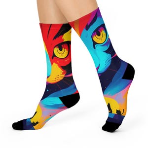 May include: A pair of colorful socks featuring a vibrant cat face design. The socks showcase a bold palette of red, yellow, blue, and black, with a stylized cat's eye and face. The socks are worn on a person's feet.