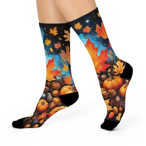 May include: A pair of crew socks featuring a vibrant autumn-themed pattern against a dark background. The design includes orange and yellow maple leaves, scattered acorns, and bright orange pumpkins, with solid black cuffs, heels, and toe sections.