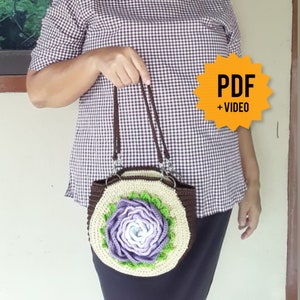 Pode incluir: Uma bolsa de m&atilde;o de croch&ecirc; marrom e bege com um grande desenho de flor roxa. A bolsa tem uma al&ccedil;a marrom e um fecho prateado. A imagem inclui o texto "PDF + VIDEO".