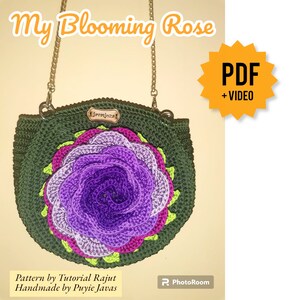 Pode incluir: Uma bolsa de m&atilde;o de croch&ecirc; verde com uma grande rosa roxa na frente. A bolsa tem uma al&ccedil;a de corrente dourada e uma etiqueta de couro marrom que diz "jrossjozs". A imagem inclui o texto "My Blooming Rose" e "PDF + VIDEO".