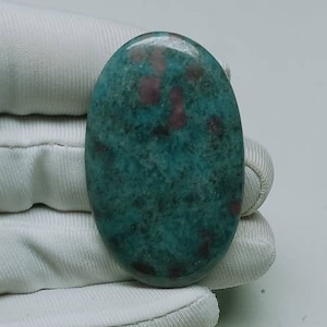May include: A green and pink oval cabochon gemstone with a speckled pattern.