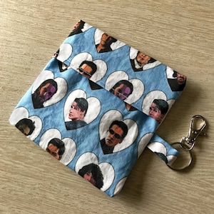 May include: A blue fabric pouch with a zipper closure and a heart pattern. The hearts feature images of a person's face. The pouch has a silver key chain attached.