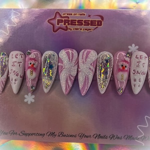 May include: Pink and white press-on nails with a snowflake design and the text "Let It Snow".