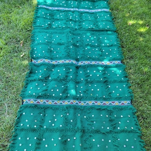 May include: A green rug with a fringe border and white circular embellishments. The rug has a geometric pattern with a band of colorful stripes.